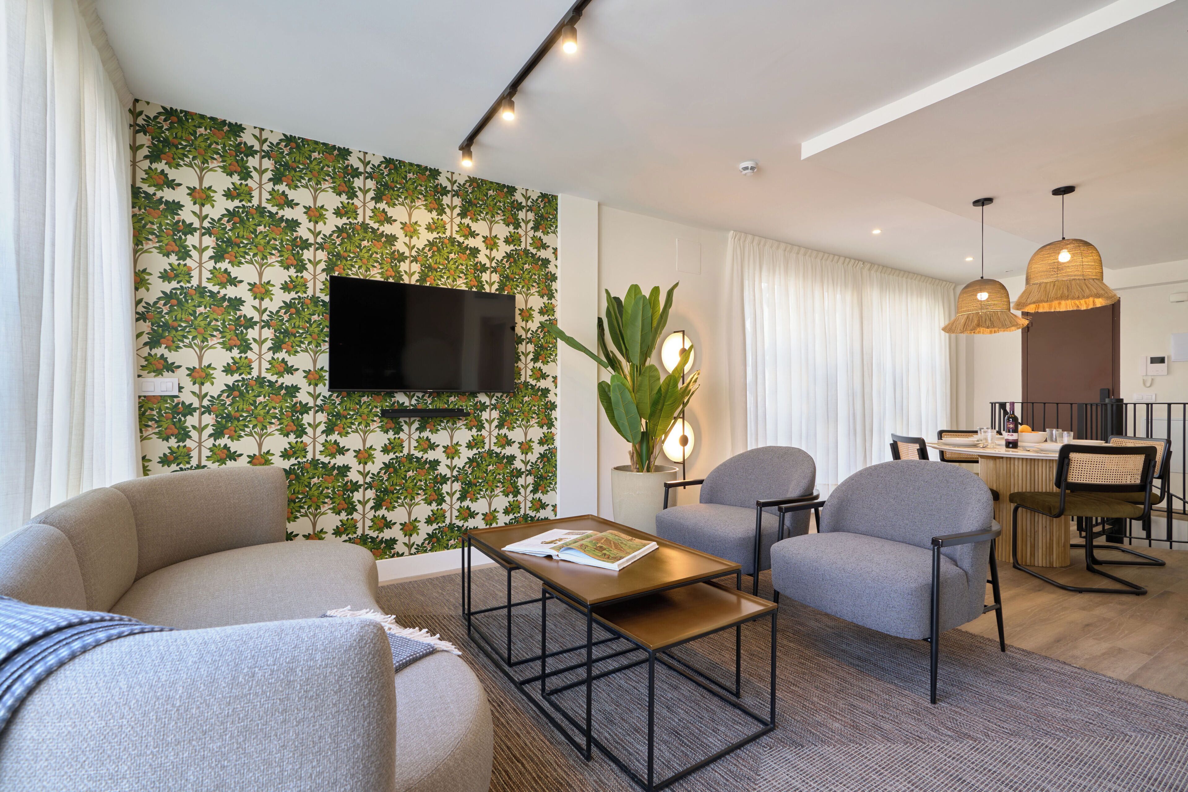 A modern living room with a flat-screen TV, two armchairs, a coffee table, and a dining area with a table and chairs.