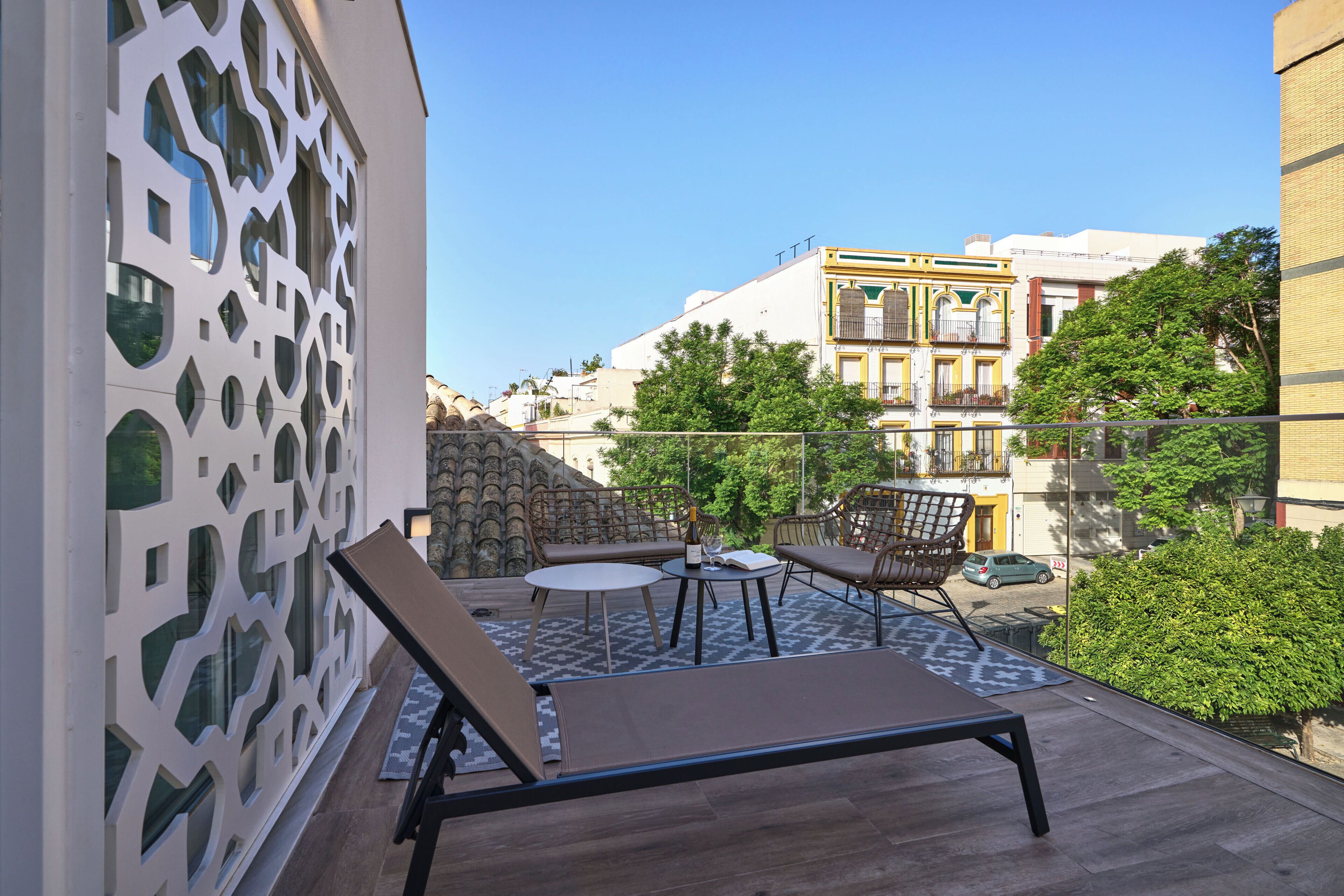 A balcony with a lounge chair, a small round table, and a patterned rug.