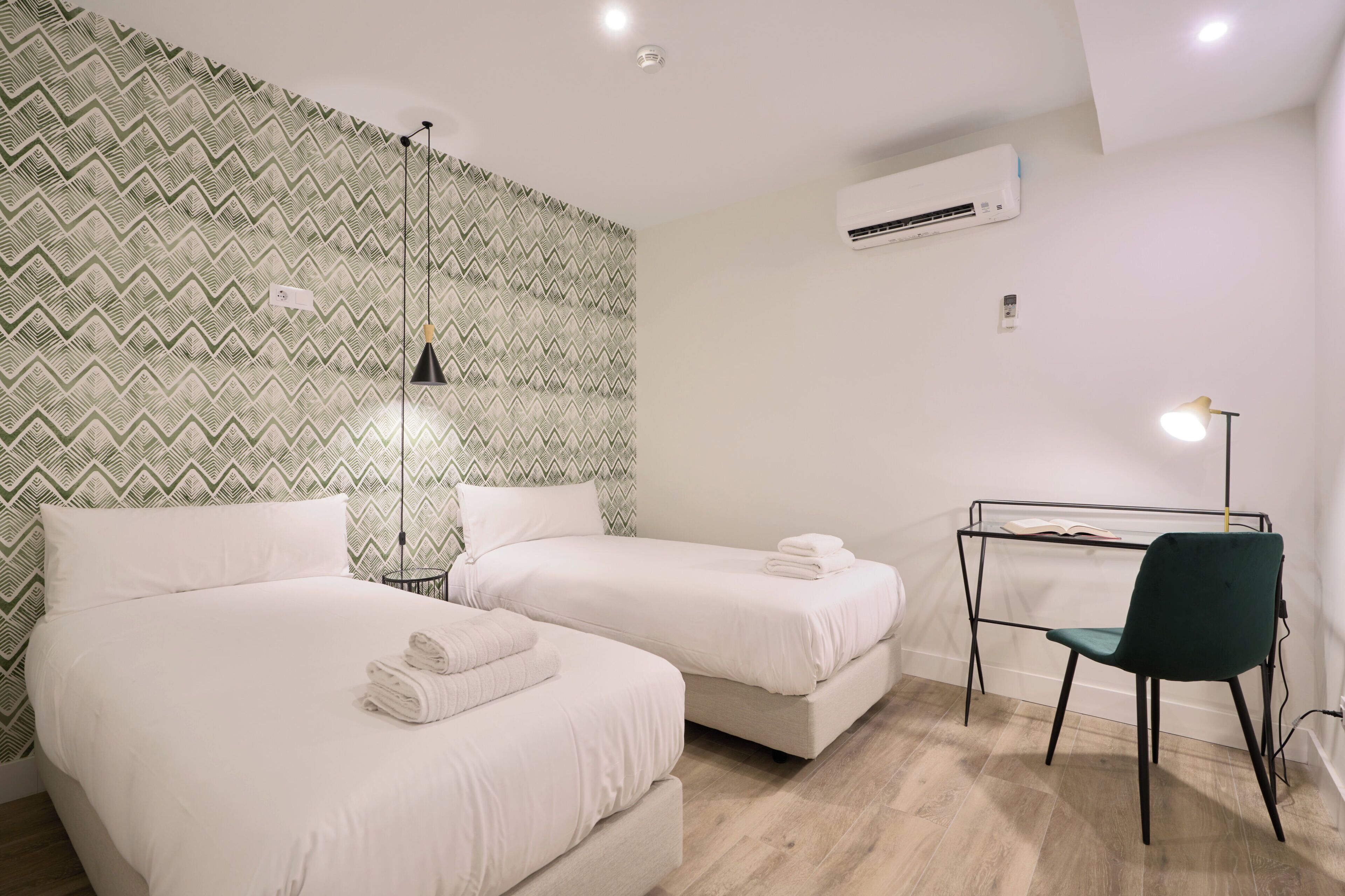 Une chambre d’hôtel avec deux lits, un bureau avec une chaise et un climatiseur fixé au mur.