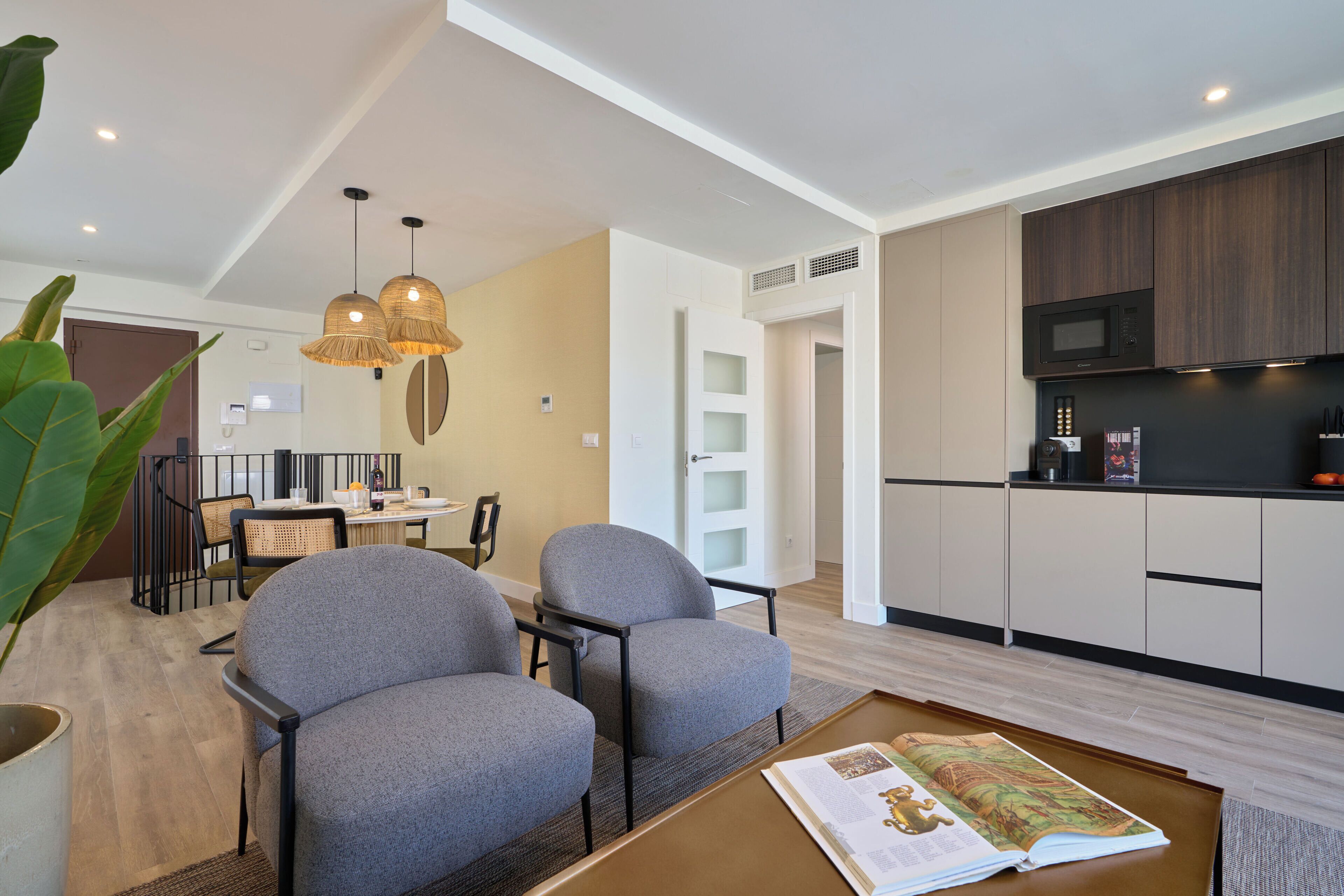 A modern living room with grey sofas, a coffee table with a magazine, and a dining area with a table and chairs.