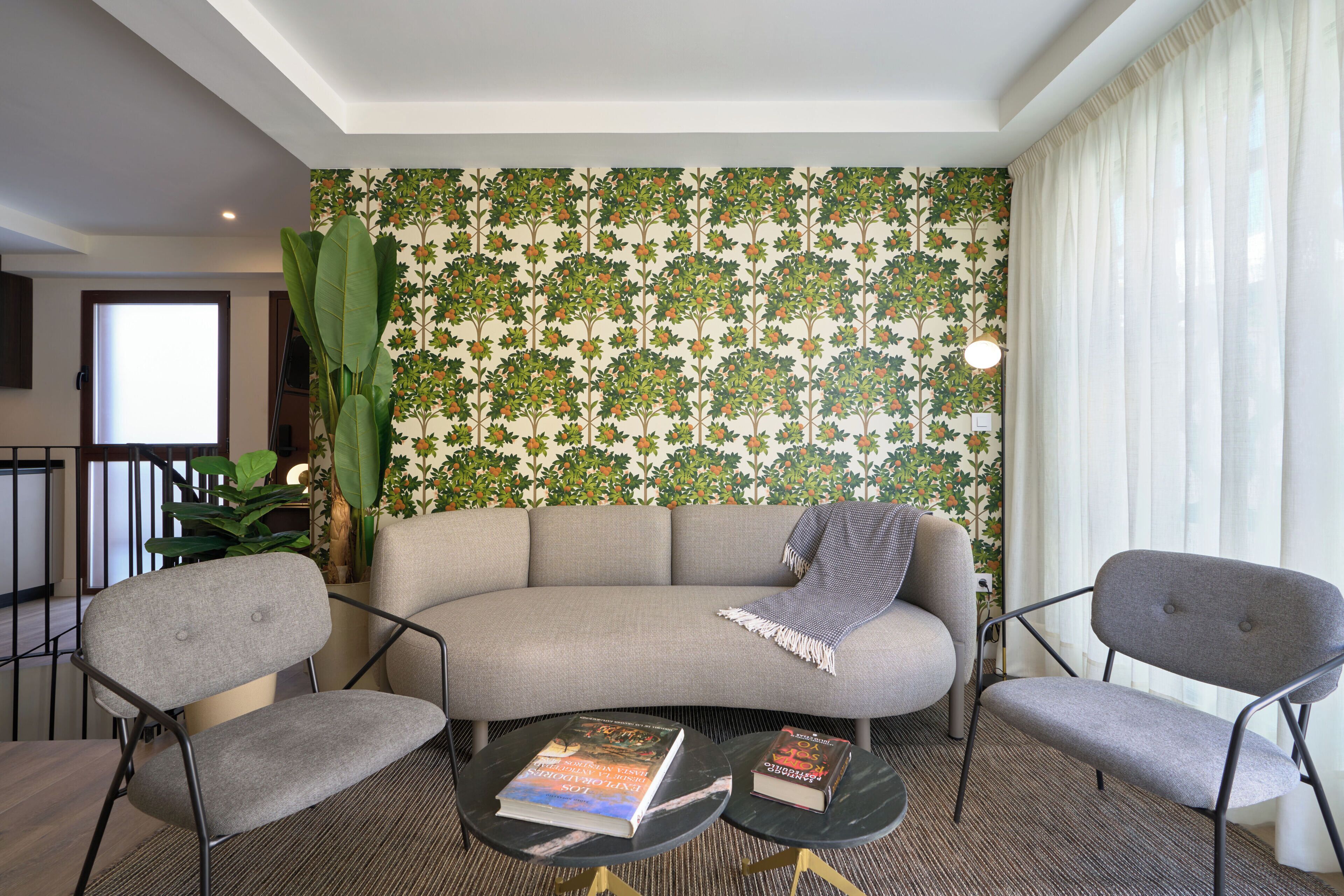 A modern living room with a sofa, two armchairs, a coffee table, and a large plant.