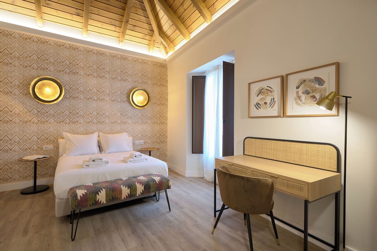 Une chambre à coucher comprenant un lit, des tables de chevet, un bureau avec une chaise et des œuvres d’art accrochées au mur.