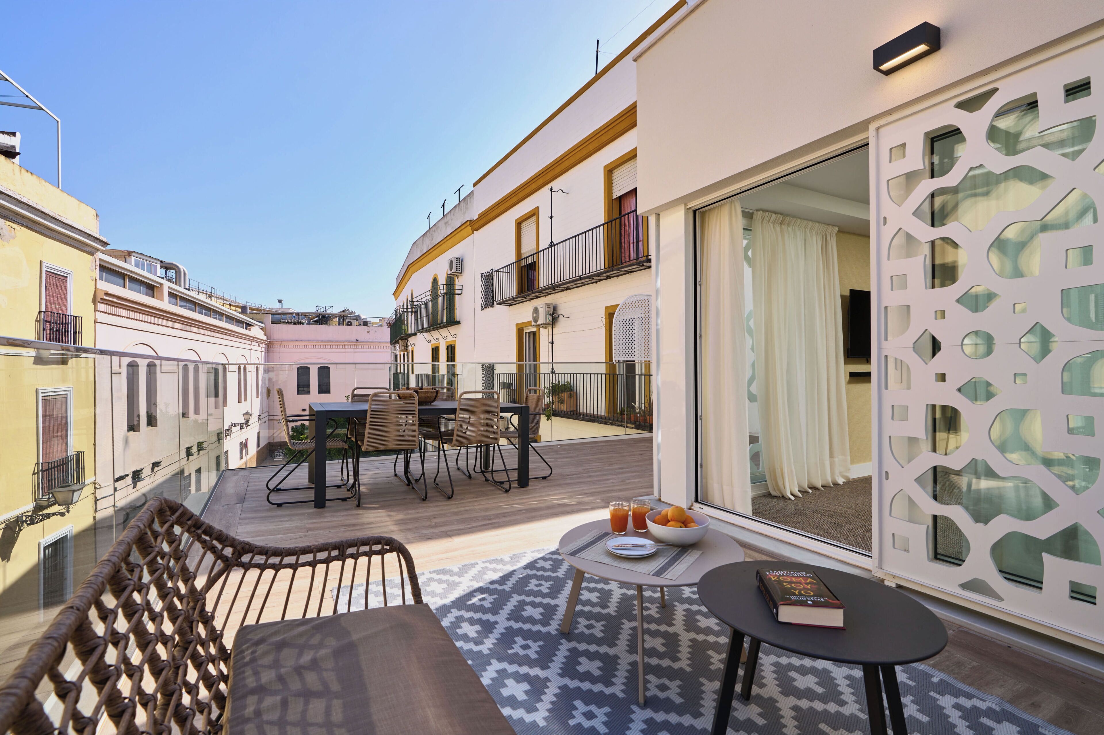 Un balcón con mobiliario exterior, una mesa de comedor y vistas a edificios cercanos.