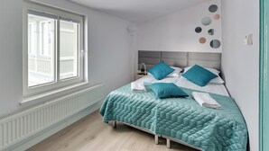 Quarto com uma grande janela, cama com colcha acolchoada e parede com espelhos redondos.