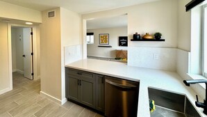 A modern kitchen with dark cabinets, a stainless steel dishwasher, and a white countertop. - Casa Fifi Coral (Miami Beach)