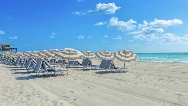 A beach with rows of sun loungers and umbrellas, a lifeguard tower, and the ocean in the background.