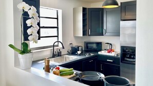 A modern kitchen with a black countertop, stainless steel appliances, and a window with white orchids.