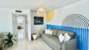 A modern living room with a grey sofa, a large abstract wall art piece, a hanging woven light fixture, and a potted plant.
