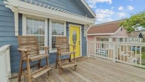 Une terrasse en bois avec deux chaises en bois et une porte jaune.