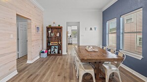 Un coin repas avec une table et des chaises en bois, une cuisine en arrière-plan et un mur sur lequel est écrit le mot « MANGER ».