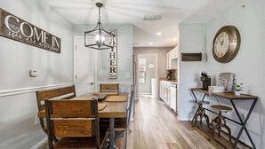 A dining area with a wooden table and chairs, a hanging light fixture, and a wall with motivational text.