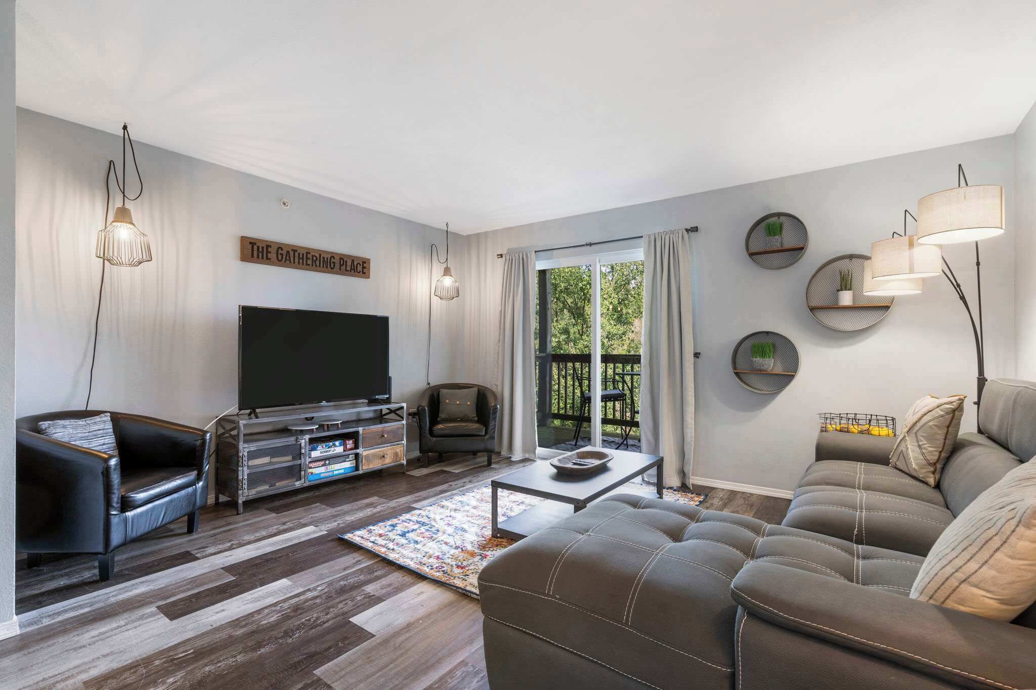 A modern living room with a flat-screen TV, leather sofas, a coffee table, and a balcony with curtains.