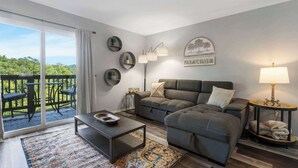 A modern living room with a sofa, coffee table, and a view of a balcony with outdoor furniture.