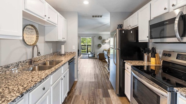 A modern kitchen with white cabinets, granite countertops, stainless steel appliances, and a view to the backyard.
