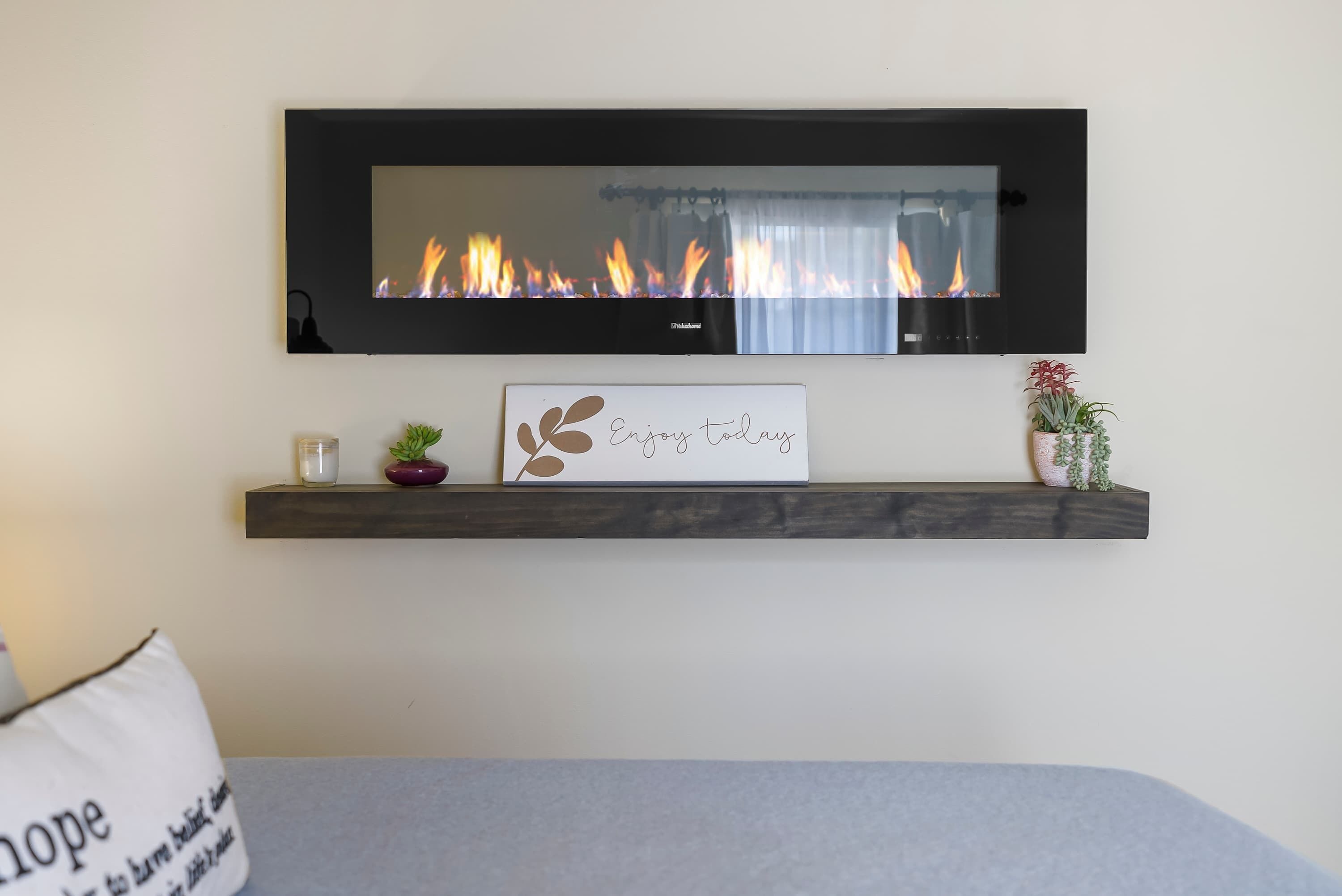Ein modernes Wohnzimmer mit Kamin, einem gerahmten Zitat über dem Kamin, einer kleinen Pflanze und einem Kissen mit Aufschrift.