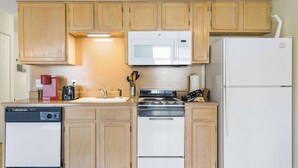 A compact kitchen with wooden cabinets, a white microwave, a stove, a dishwasher, and a refrigerator. - Fall Creek Abby in the Ozarks | Year-round fishing (Branson)