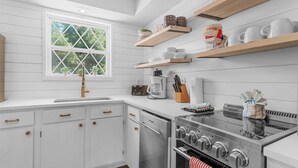 A kitchen with white cabinetry, a stainless steel stove, and wooden shelves above. - Enchanted Woods Retreat / Pools / Hot Tub (Branson)