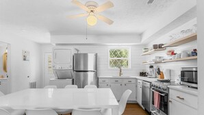 A modern kitchen with white cabinetry, a stainless steel refrigerator, a built-in oven, and a dining table with chairs. - Enchanted Woods Retreat / Pools / Hot Tub (Branson)