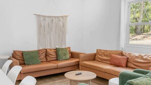 Ein Wohnzimmer mit zwei braunen Ledersofas, grünen Kissen, einem runden Holztisch und einer Wandbehagung aus Makramee.