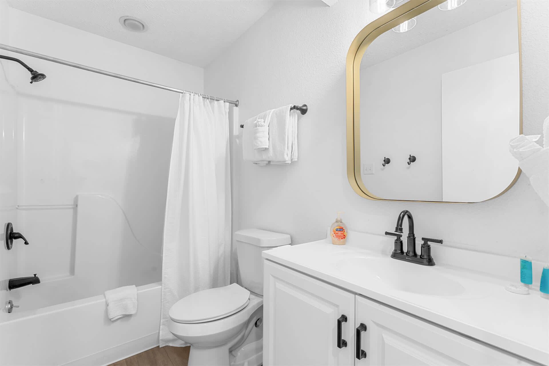 A bathroom with a shower, toilet, sink, and a mirror.