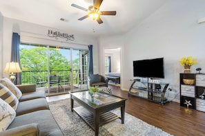 A modern living room with a sofa, coffee table, TV, and a balcony with outdoor furniture.