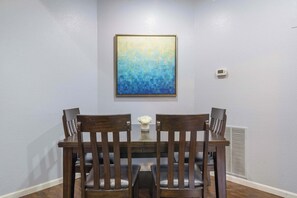 Un comedor con mesa y sillas, un cuadro en la pared y un termostato.