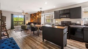 A modern kitchen with black cabinets, a microwave, and a dishwasher. There is a dining area with a table and chairs, and a blue ottoman. - Best of Branson Duo - By Silver Dollar City (Branson)