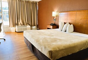 Quarto de hotel com uma cama grande, uma mesa de cabeceira com abajur, uma janela com cortinas e vista para o exterior.