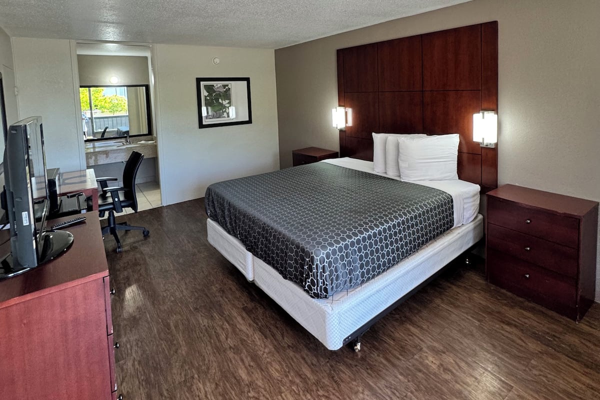 Habitación de hotel con cama, escritorio, silla, televisión y baño visible a través de una puerta abierta.