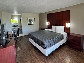 Quarto de hotel com cama, escrivaninha, cadeira, televisão e banheiro visível por uma porta aberta.