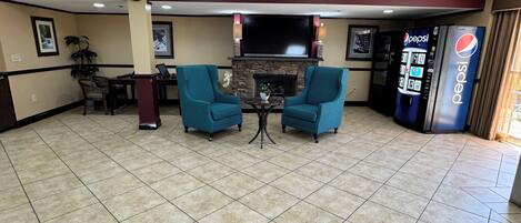 A lobby with two teal armchairs, a stone fireplace, a clock, and a Pepsi vending machine.