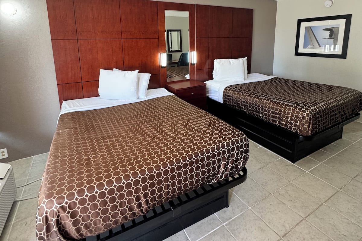 Habitación de hotel con dos camas, cabecera de madera, un espejo y un cuadro en la pared.
