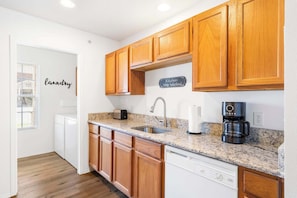 A kitchen with wooden cabinets, a granite countertop, a sink, a toaster, a coffee maker, and a dishwasher.