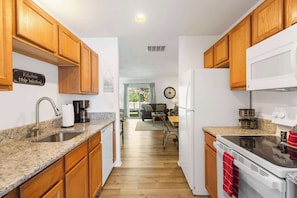 A kitchen with wooden cabinets, a granite countertop, a sink, a stove, and a dining area with a table and chairs.