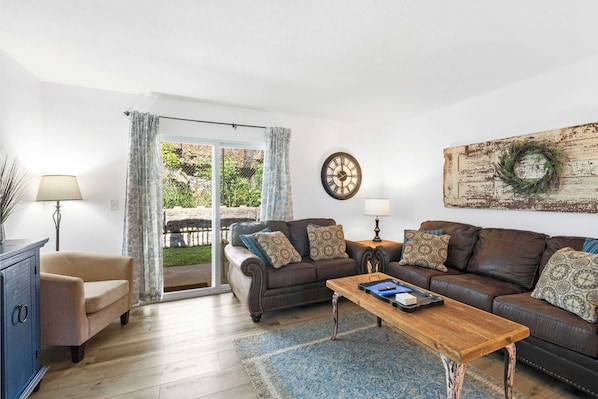 A living room with a brown leather sofa, a wooden coffee table, a blue rug, and a large wall clock.