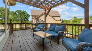 A covered outdoor deck with wicker furniture and a glass table. - Hickory Hideaway w/ Communal Pool Access (Hollister)