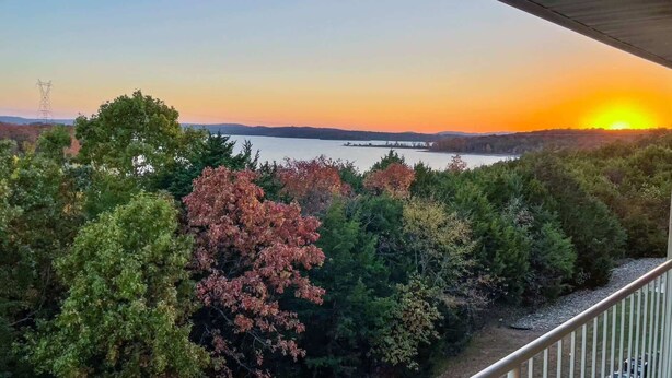 Een balkon met uitzicht op een zonsondergang boven een meer, omringd door bomen.