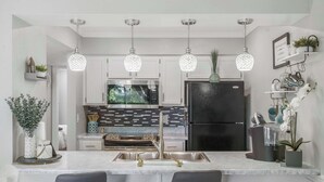 Une cuisine moderne avec des meubles blancs, un réfrigérateur noir, un four encastré et des luminaires suspendus.