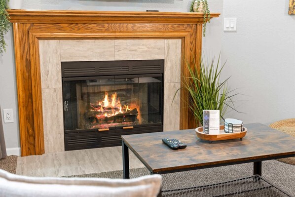 A fireplace with a mantel, a remote control, and a tray with a book and a plant.