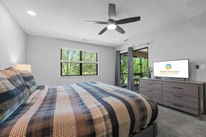 Un dormitorio con cama, ventilador de techo, televisor, ventana y cómoda.