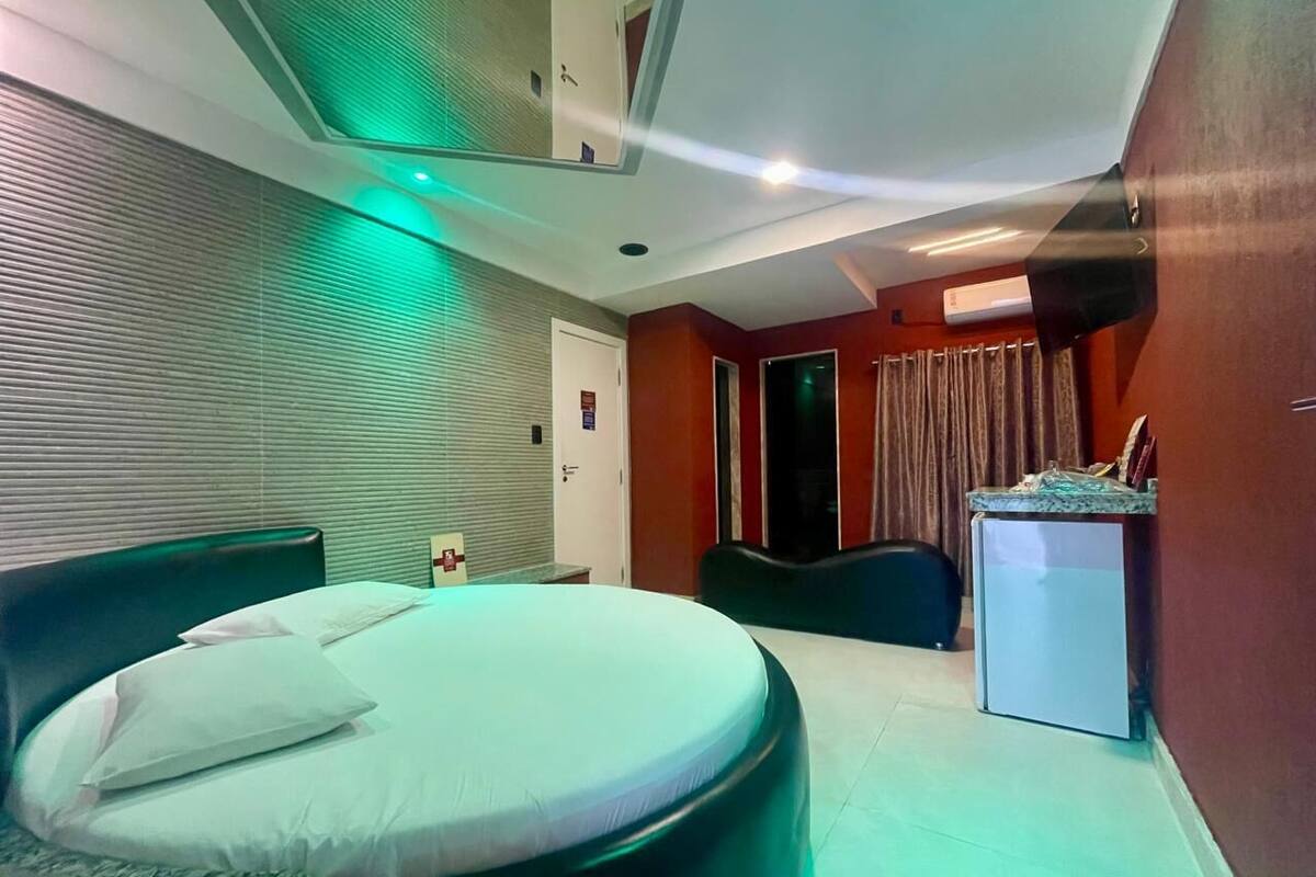 A hotel room with a bed, a desk, a refrigerator, and a window with curtains.