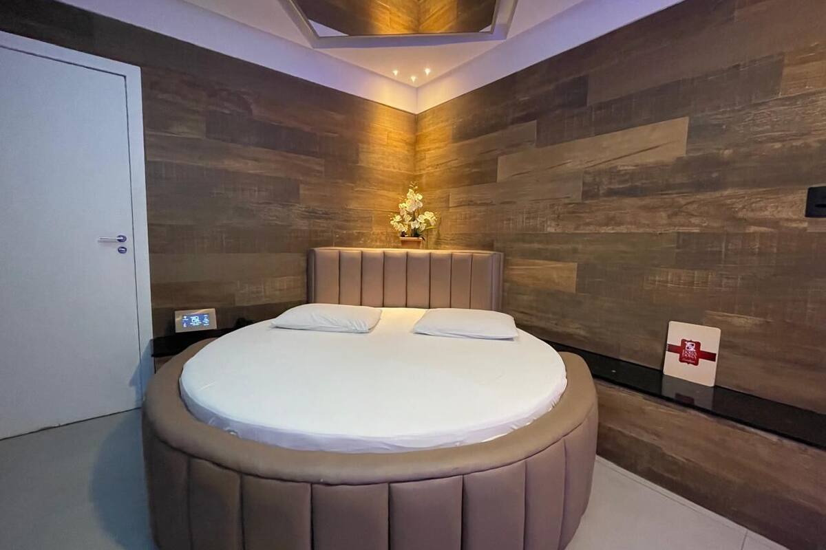A circular bed with a headboard in a modern room with wooden walls and recessed lighting.