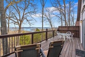 A wooden deck with a table and chairs, overlooking a body of water and trees.
