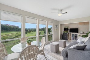 Relax in this stylish living room with a golf course view, featuring a dining table, comfortable sofa, and flat-screen TV.