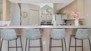Una cocina moderna con una isla central, taburetes de bar, un reloj y vistas al exterior.