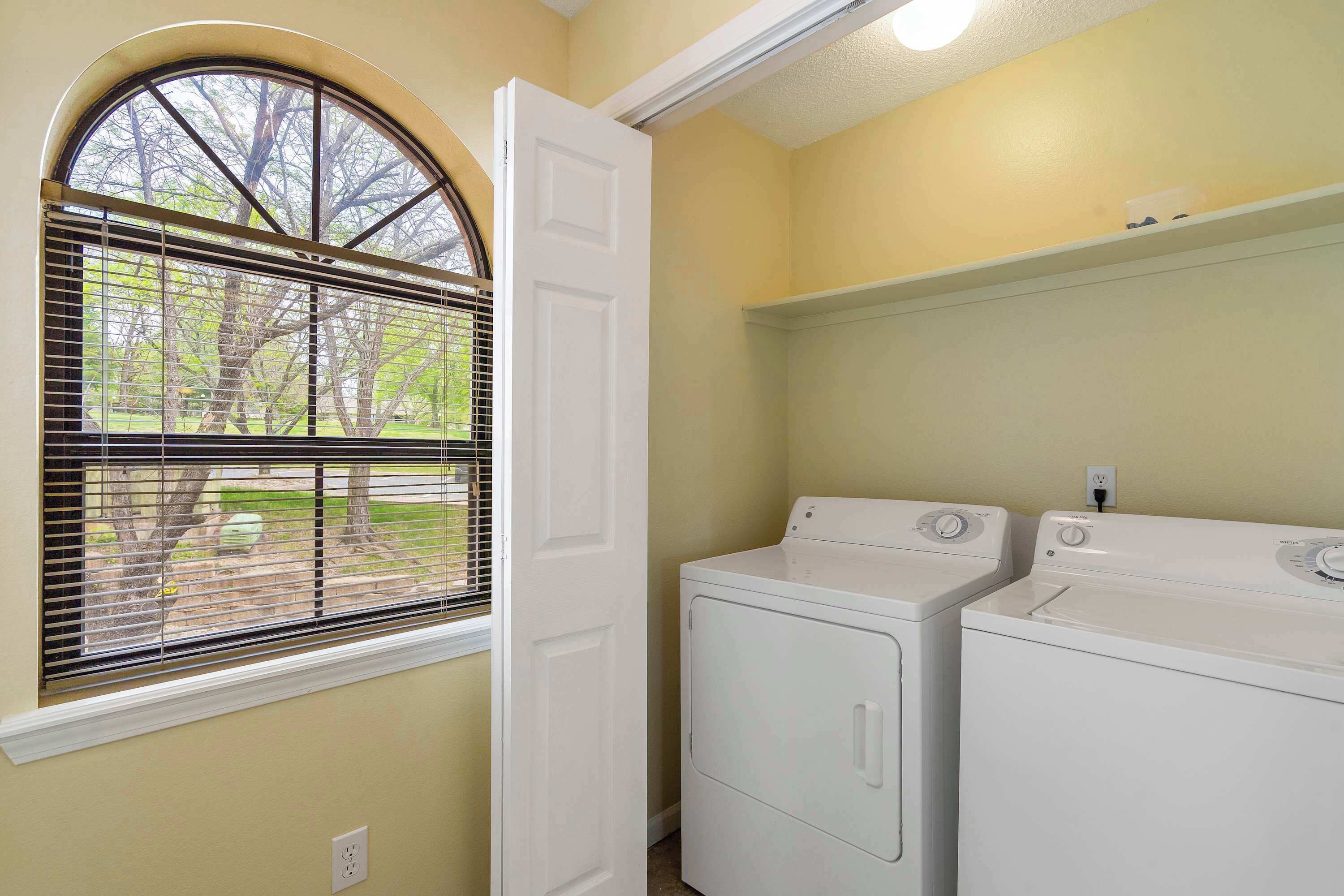 Un cuarto de lavandería con dos lavadoras y secadoras blancas, una ventana con persianas y una puerta.