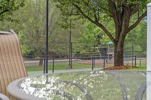 Un parc avec un terrain de tennis entouré de clôtures, un arbre et un banc.