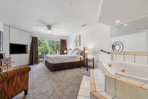 Une chambre d’hôtel comprenant un lit, une télévision, un canapé, une salle de bain avec baignoire et un balcon avec des rideaux.