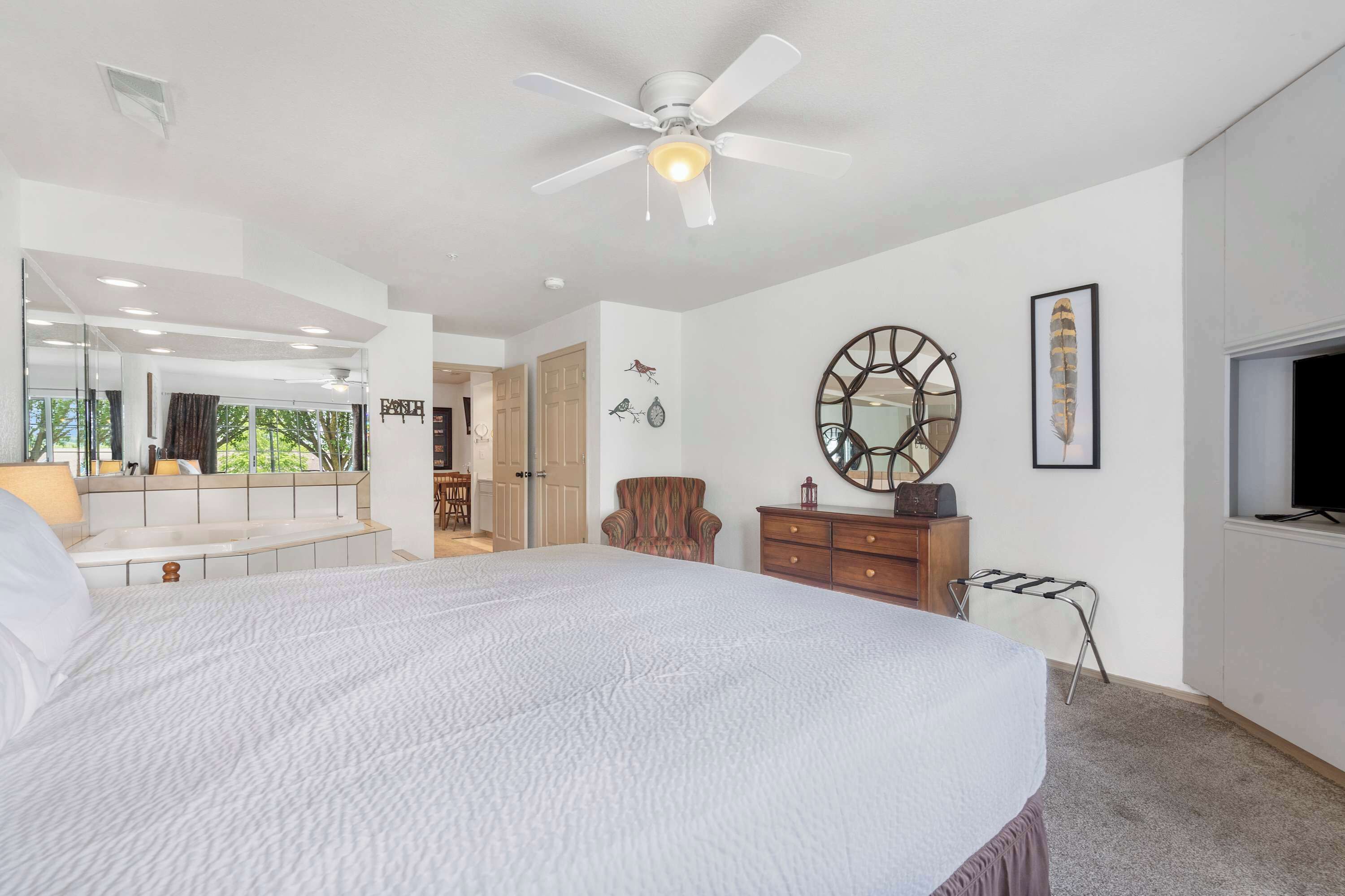 Un dormitorio amplio con una cama grande, ventilador de techo, espejo y vistas al exterior.
