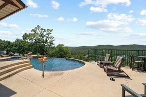 A swimming pool with steps leading into it, surrounded by lounge chairs and a view of hills. - Stone Cliff Relaxation w/ Resort Amenities! (Branson)